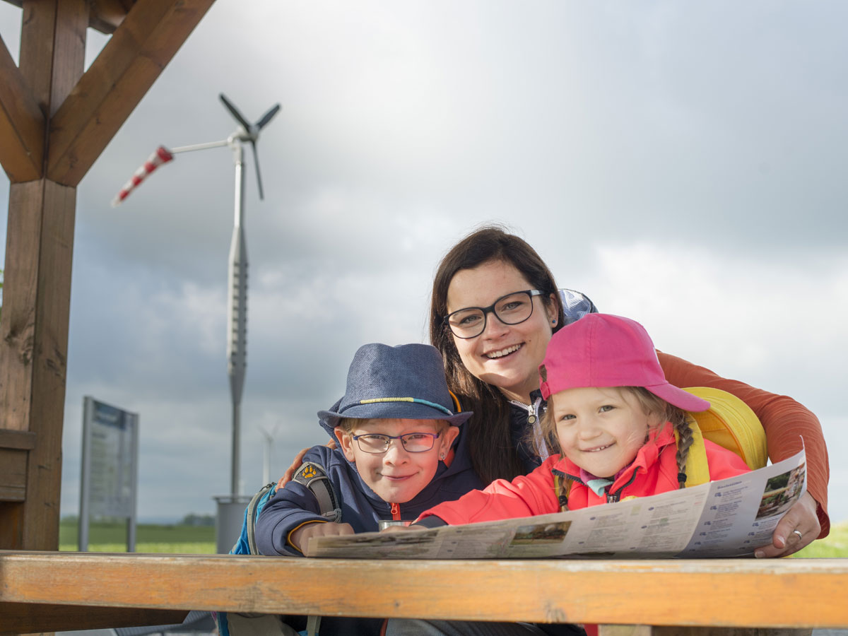 Mutter mit Sohn und Tochter auf dem SachsenEnergie-Erlebnispfad vor einem Windrad