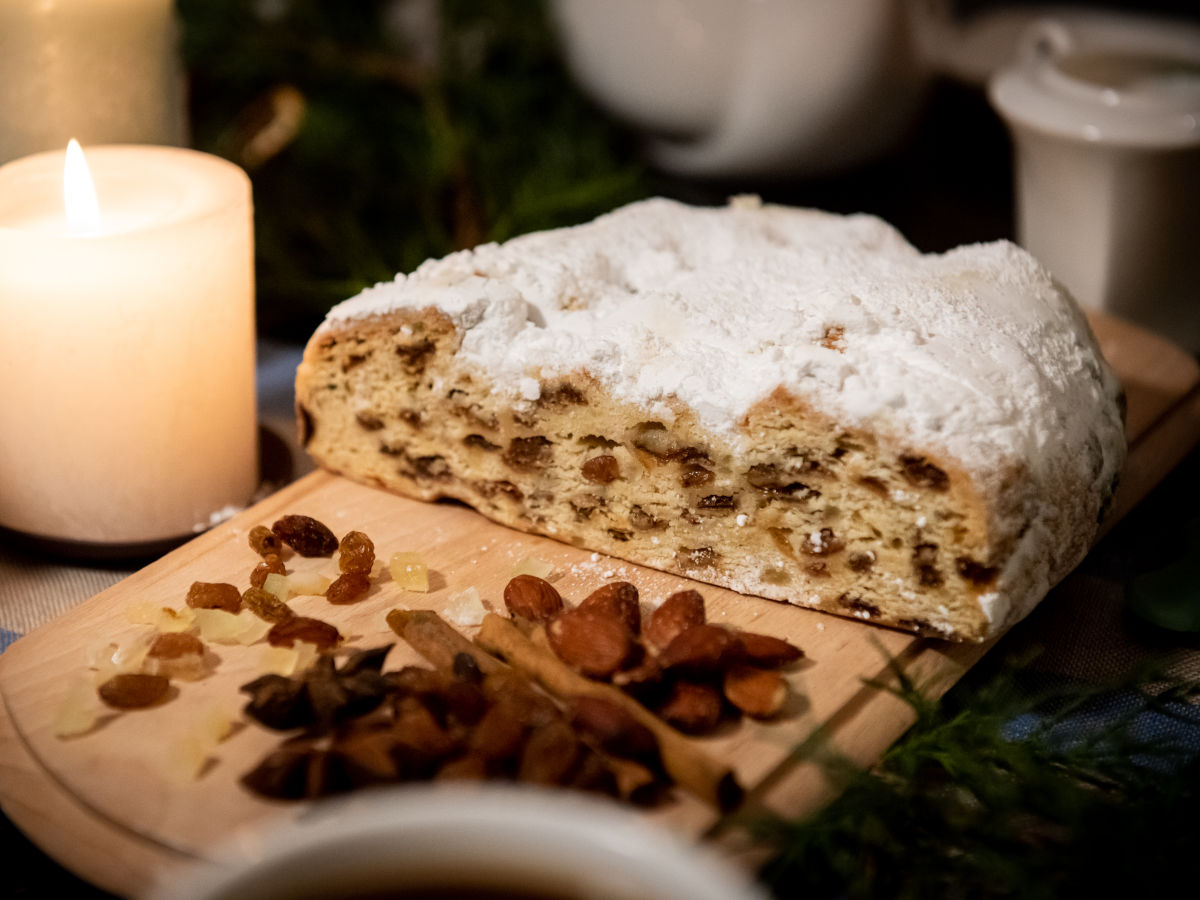 Ein angeschnittener Weihnachtsstollen liegt auf einem Holzbrett. Daneben steht eine brennende Stumpenkerze.