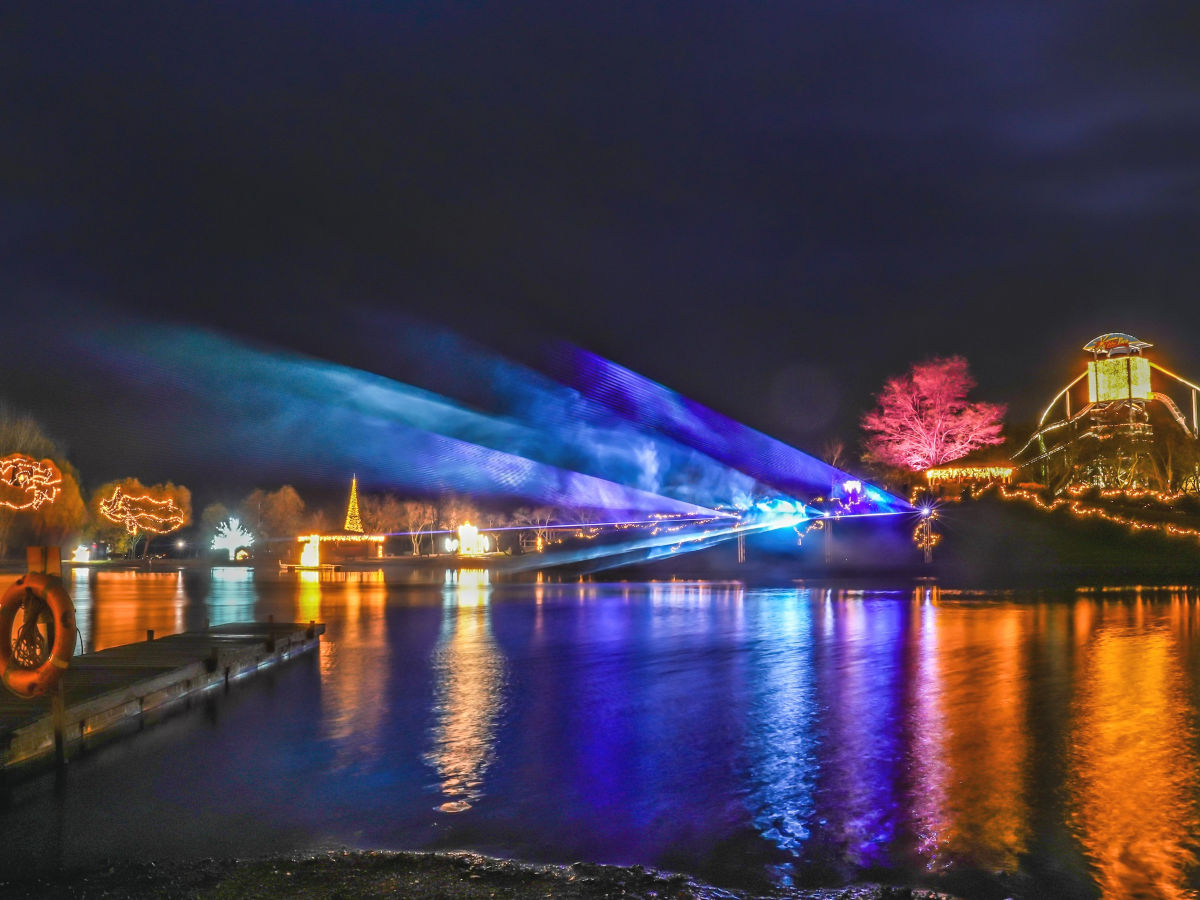 Die Oberfläche eines Sees wird nachts von blauen und roten Laserstrahlen erleuchtet.