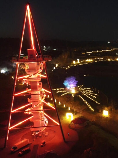 Eine hohe Stahlturmkonstruktion, von der Röhrenrutschen in jeder Etage abgehen, ist nachts in rotes Licht getaucht.
